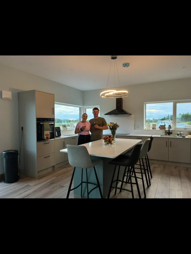 Image posted by seefin_selfbuild on 25 August 2026. It can be Modern kitchen with gray cabinets, black hood, white island with flowers, and four bar stools in neutral and black colors under circular LED pendant light.